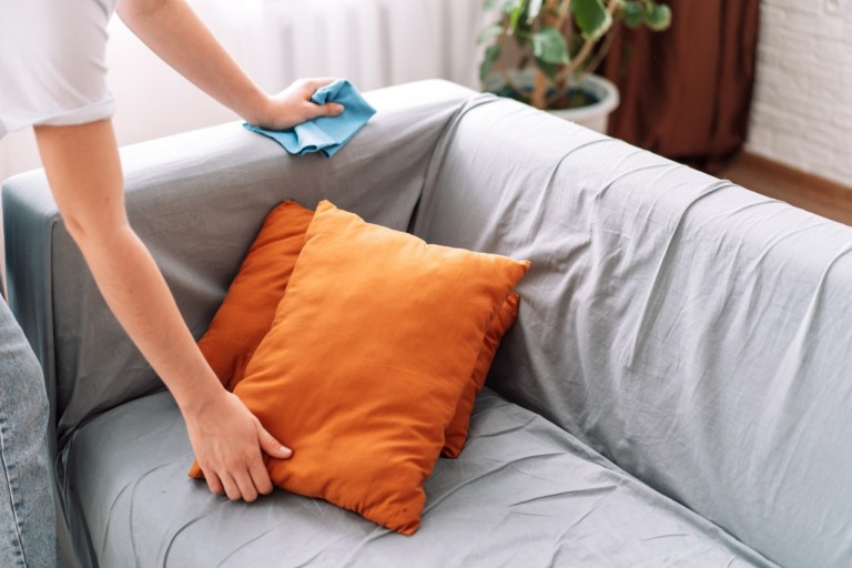 Lady cleans the sofa with a blue rag.